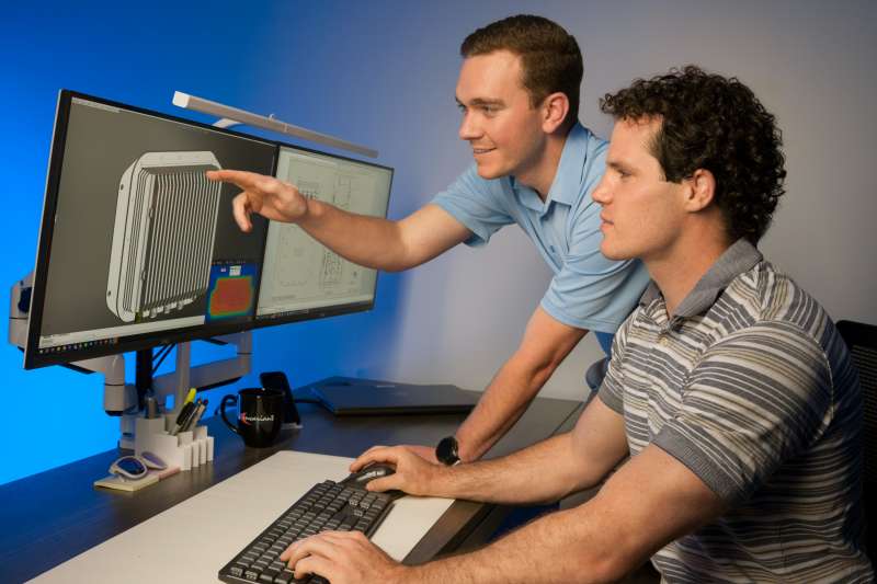 Two engineers review progress on a 3D computer aided design model shown on a computer display.
