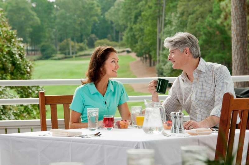 A couple looks at eachother romatically while dining at a golf course country club.