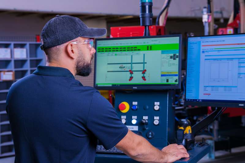 An operator stands at the control panel for an automated window framing machine.