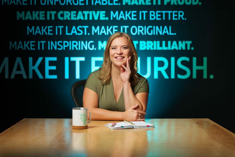 Environmental portrait showing a woman sitting in front of a wall stenciled with motivational quotes.