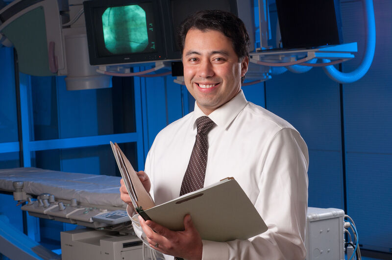 Environmental portrait of a cardiologist standing in a hospital operating room.
