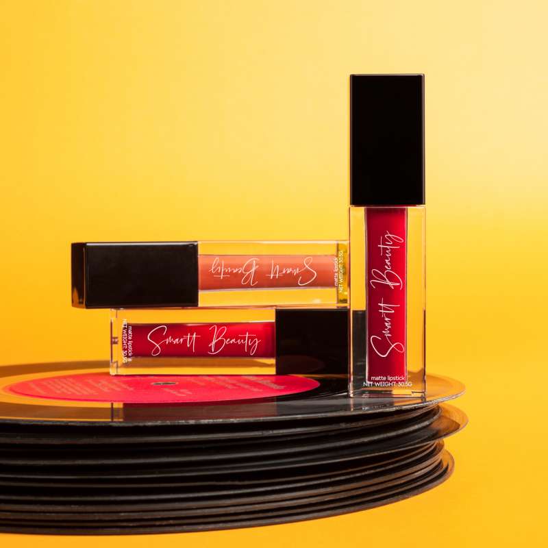 Lipstick encased in glassy square tubes lay on a stack of retro 45 rpm records against a golden yellow background.